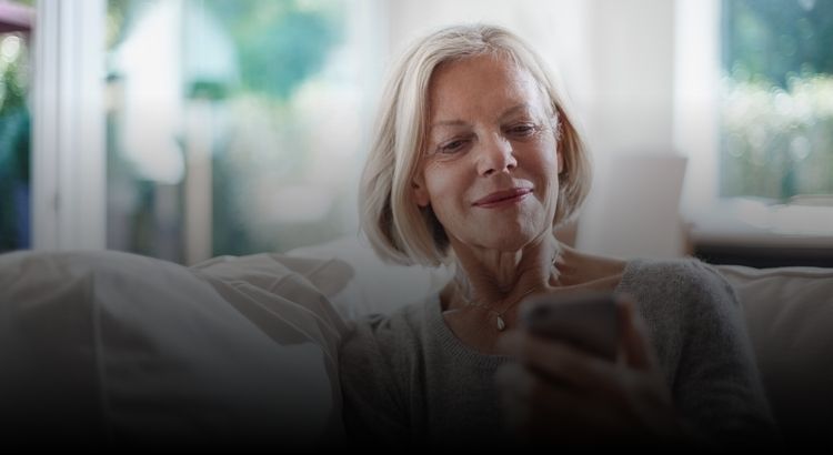 Woman sitting on couch smiling while looking at phone